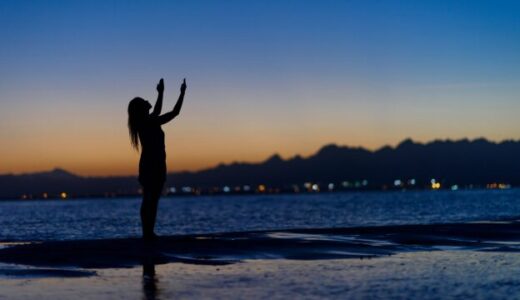 夕方の空に向かって両手をあおぐ女性の横姿