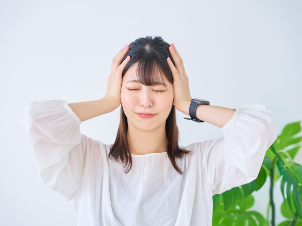 両手で頭を抱えて悩む白い服の女性